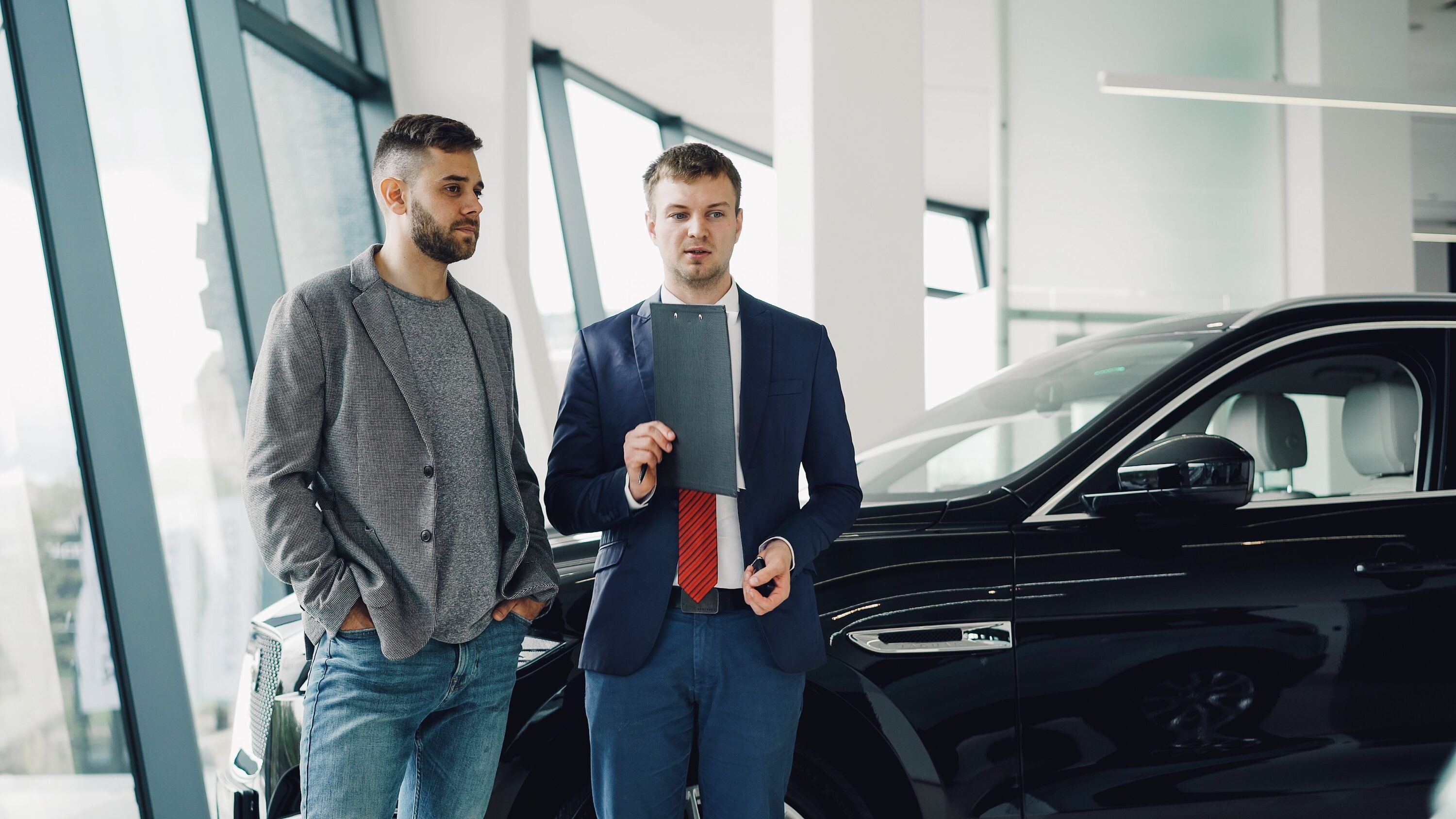 Car dealership marketing consultant discussing sales strategy next to a modern vehicle in a showroom